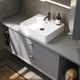 Baderomsinspirasjon med skråvegger, grå servantskap og overskap, spesialtilpassede benkeplater, moderne firkantet bordstående servant, firkantet speil med lys, rå betongvegger og gulv gir et urbant uttrykk