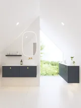 Elegant og moderne baderomsinspirasjon med skråtak, vegghengte blå servantskap og underskap, rund servant med messingarmatur, opplyst speil og naturlig lysinnfall