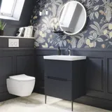 Baderomsinspirasjon med mørkeblå veggpaneler, romantisk blomstrete tapet, mørkeblå servantskap med myke former og et vakkert rundt speil med lys som skaper et vintage uttrykk