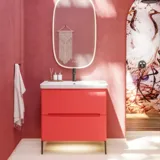 Baderomsinspirasjon med røde vegger, mykt formede røde servantskap og høyskap, elegant hvit servant og et vakkert ovalt speil med lys som sammen med de naturlige omgivelsene skaper et vintage uttrykk