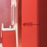 Baderomsinspirasjon med røde vegger, mykt formede røde servantskap og høyskap, elegant hvit servant og et vakkert ovalt speil med lys som sammen med de naturlige omgivelsene skaper et vintage uttrykk